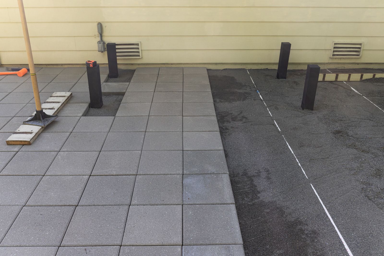 Empty tiled walkway beside a paved road with black bollards and a beige wall.