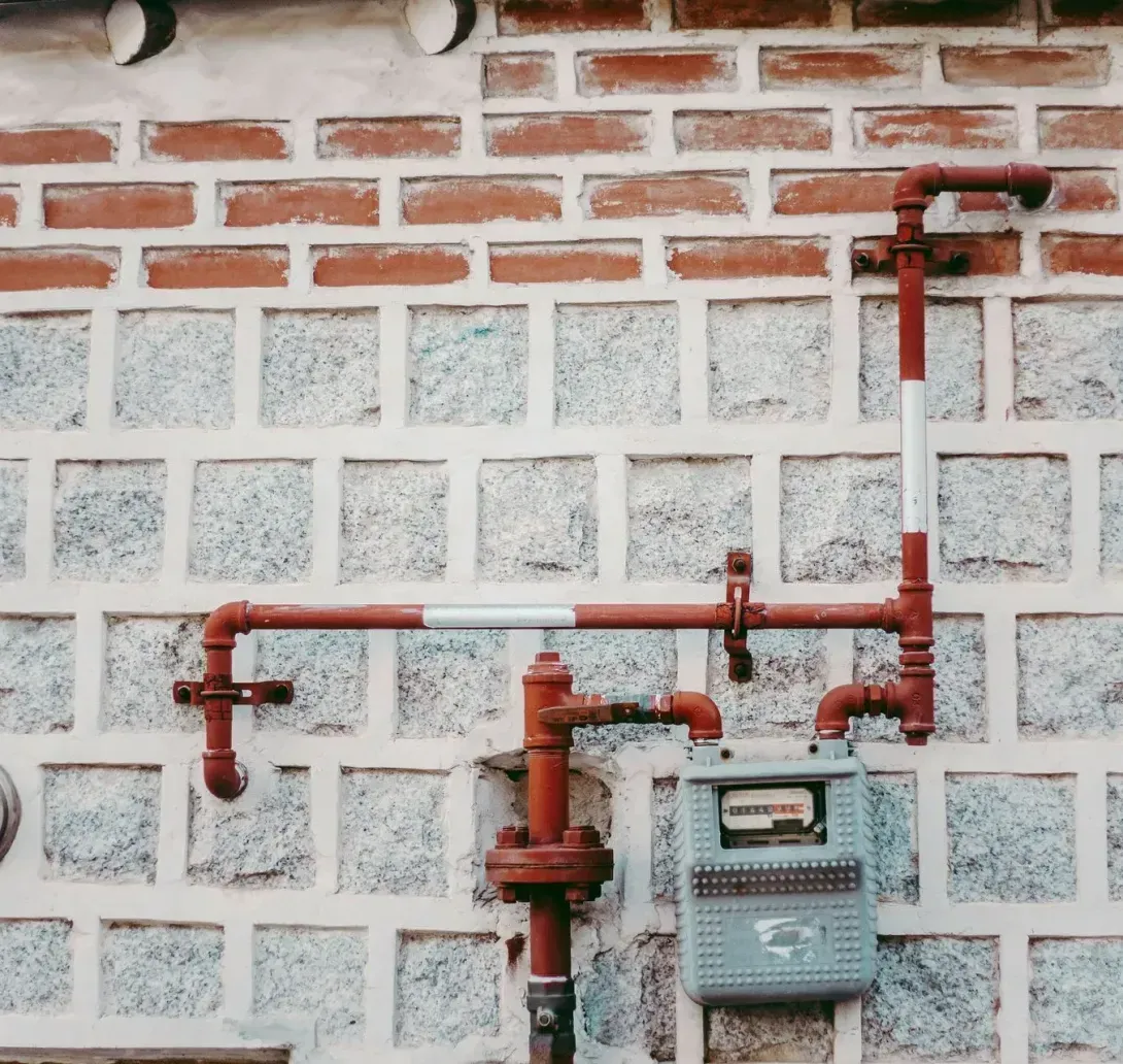 A gray utility meter mounted on a stone wall with an intricate network of red pipes running across the facade.
