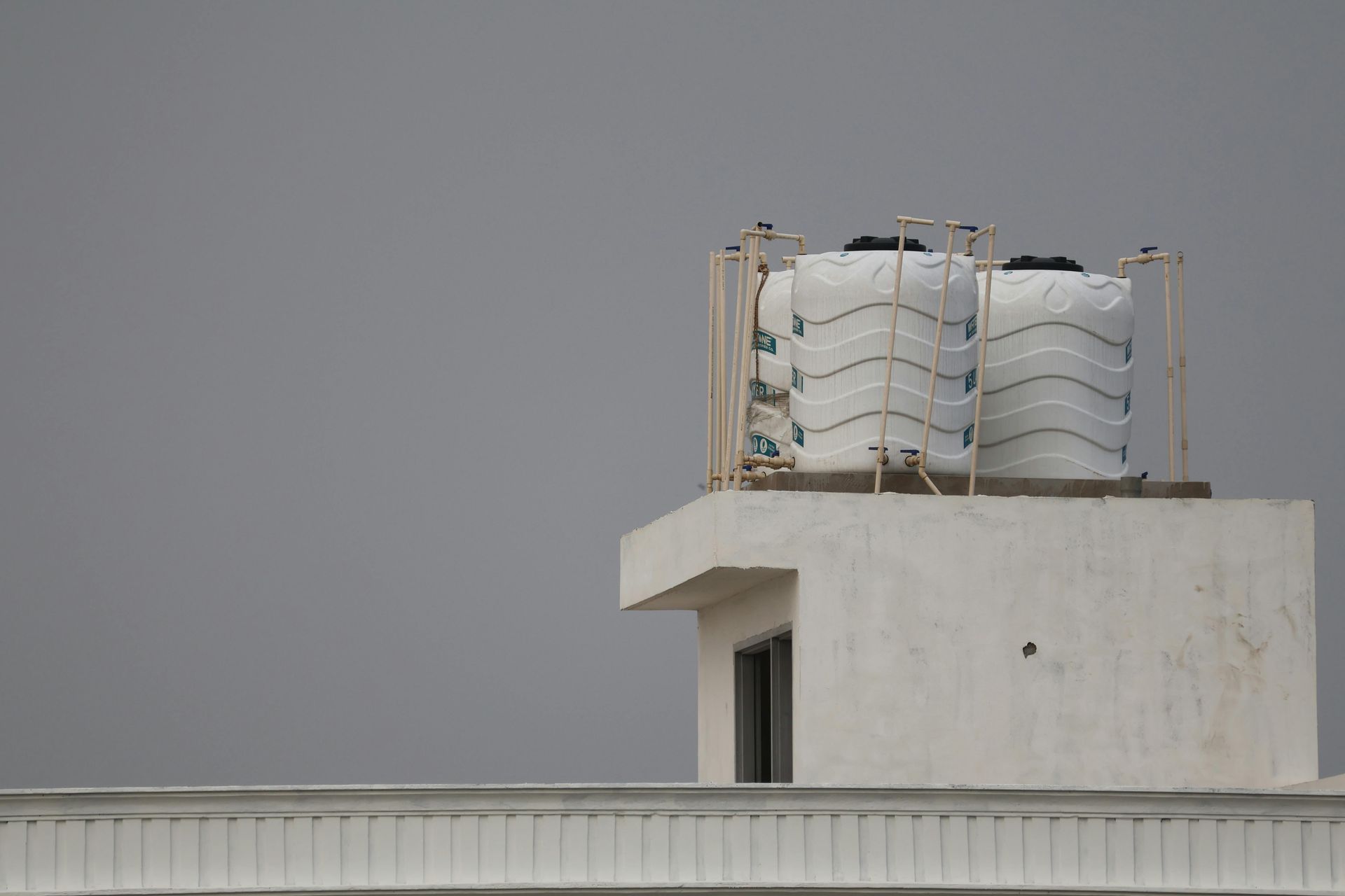 Two white water tanks sit on top of a flat-roofed building against a plain, overcast gray sky.