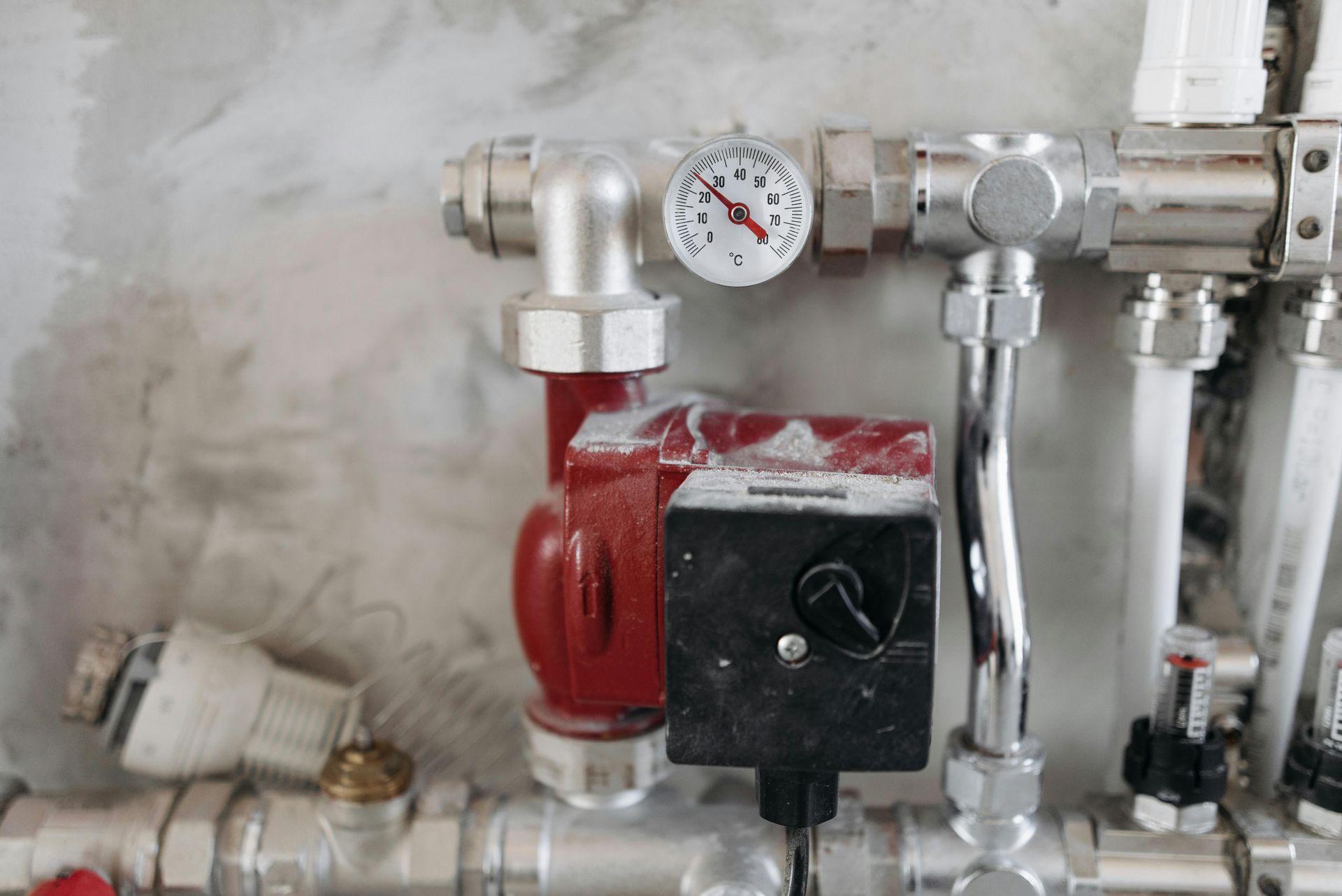 A red circulation pump and a pressure gauge mounted on a manifold system with connected white pipes against a wall.