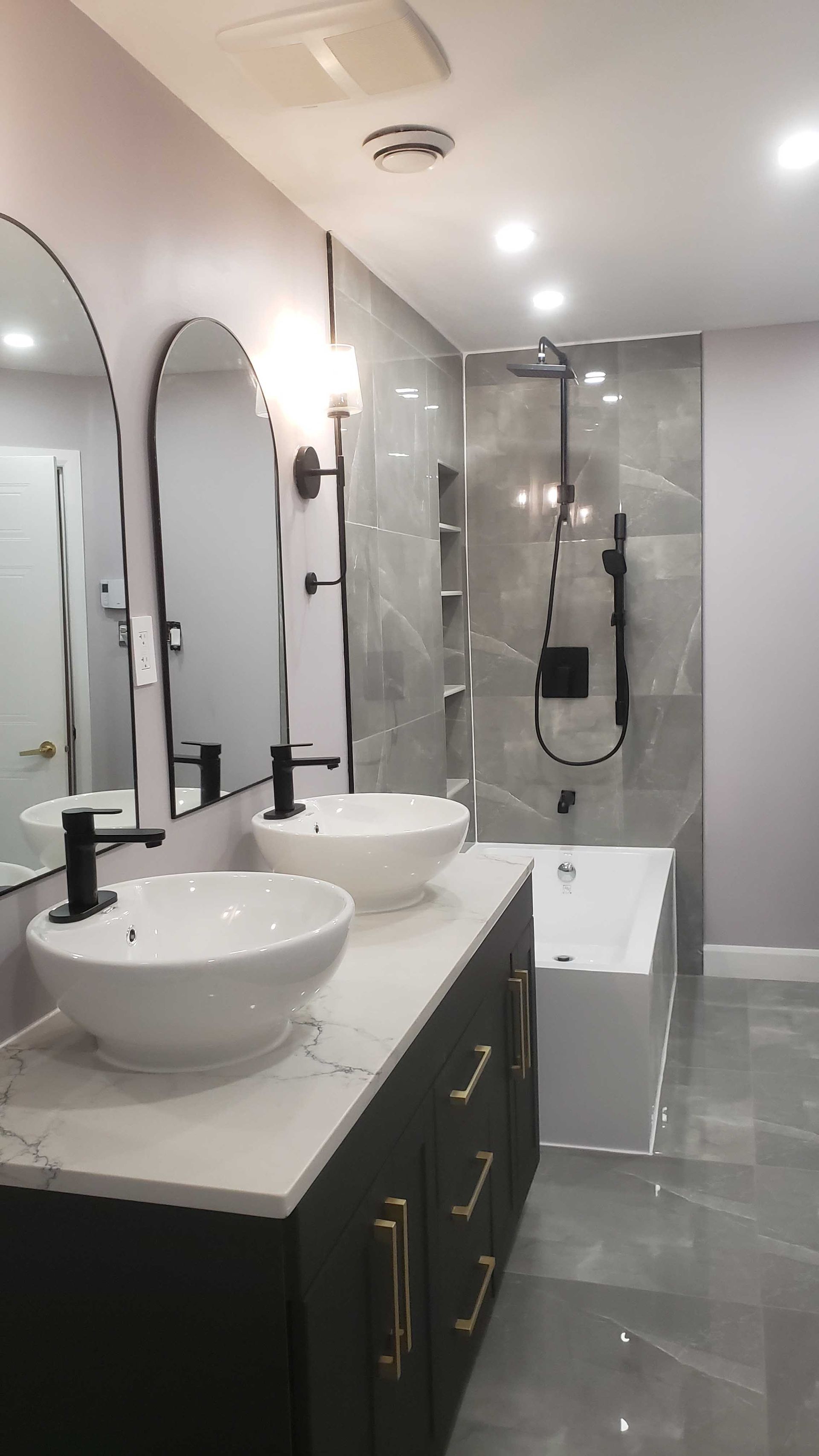Salle de bains moderne avec double vasque, miroirs arqués, meuble-lavabo noir et douche vitrée.