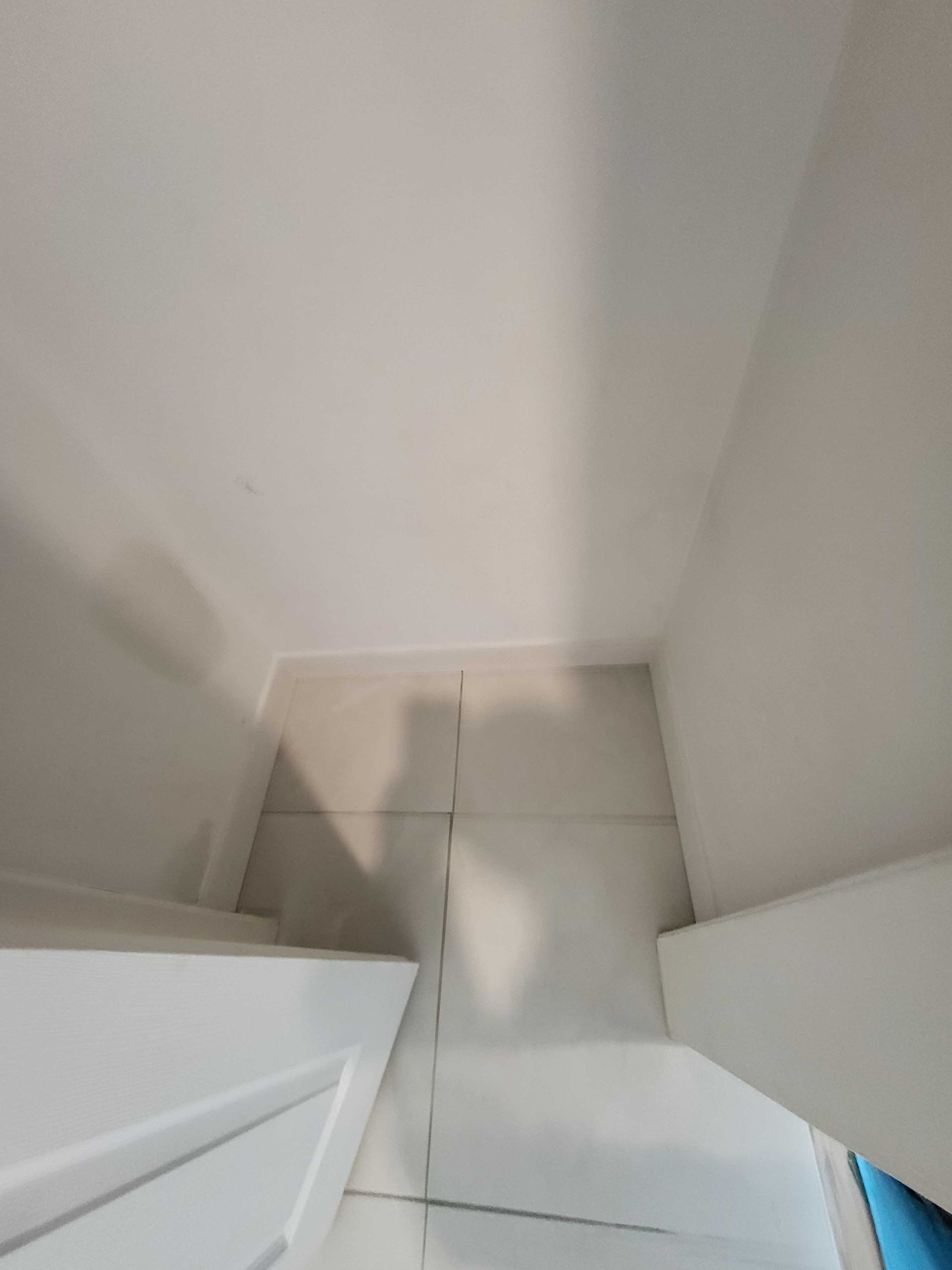 Coin étroit d'un couloir blanc avec un sol carrelé beige et des portes blanches ouvertes des deux côtés