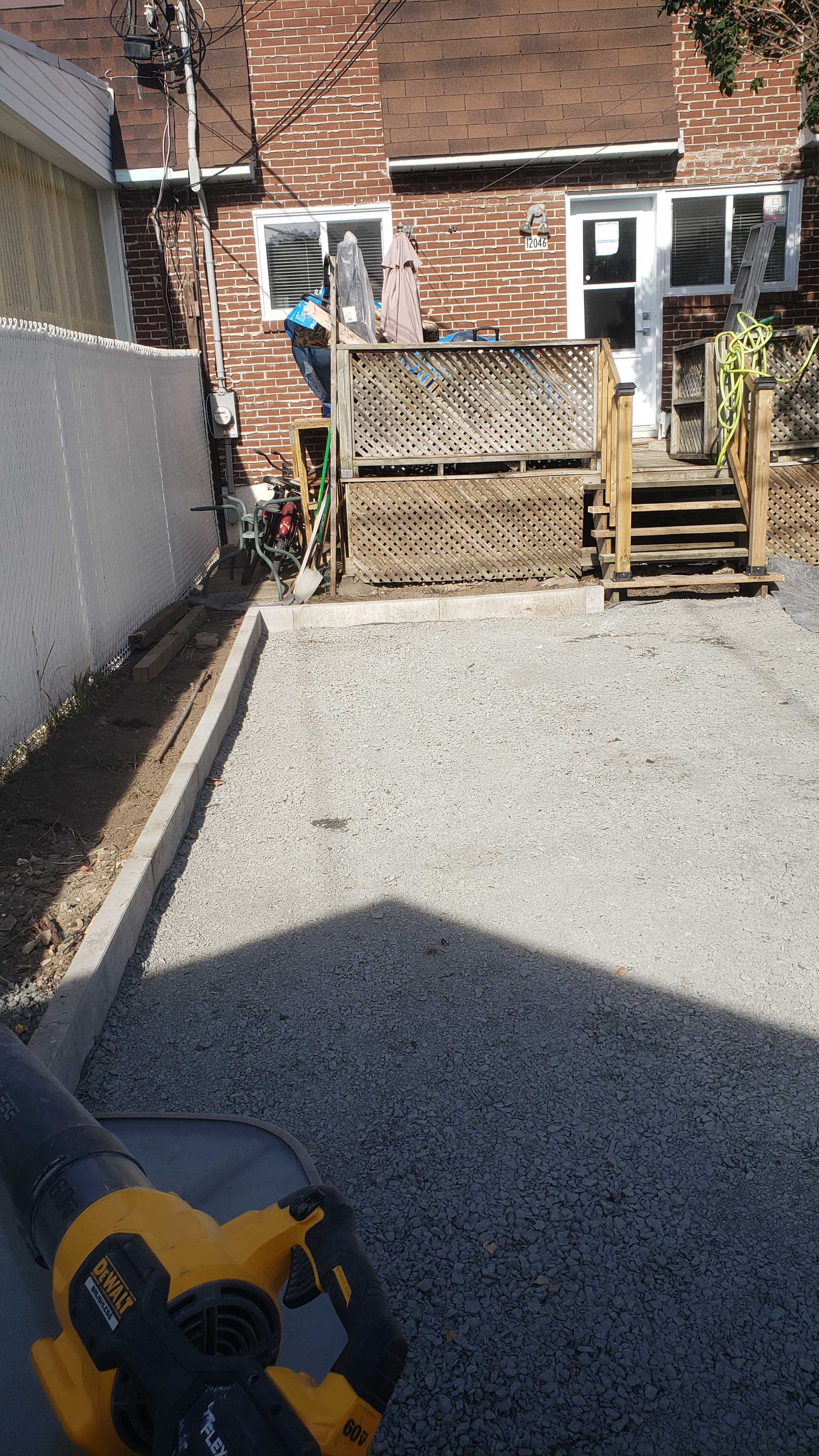Allée de gravier devant une maison en briques avec un portail en bois et des marches menant à la porte arrière.