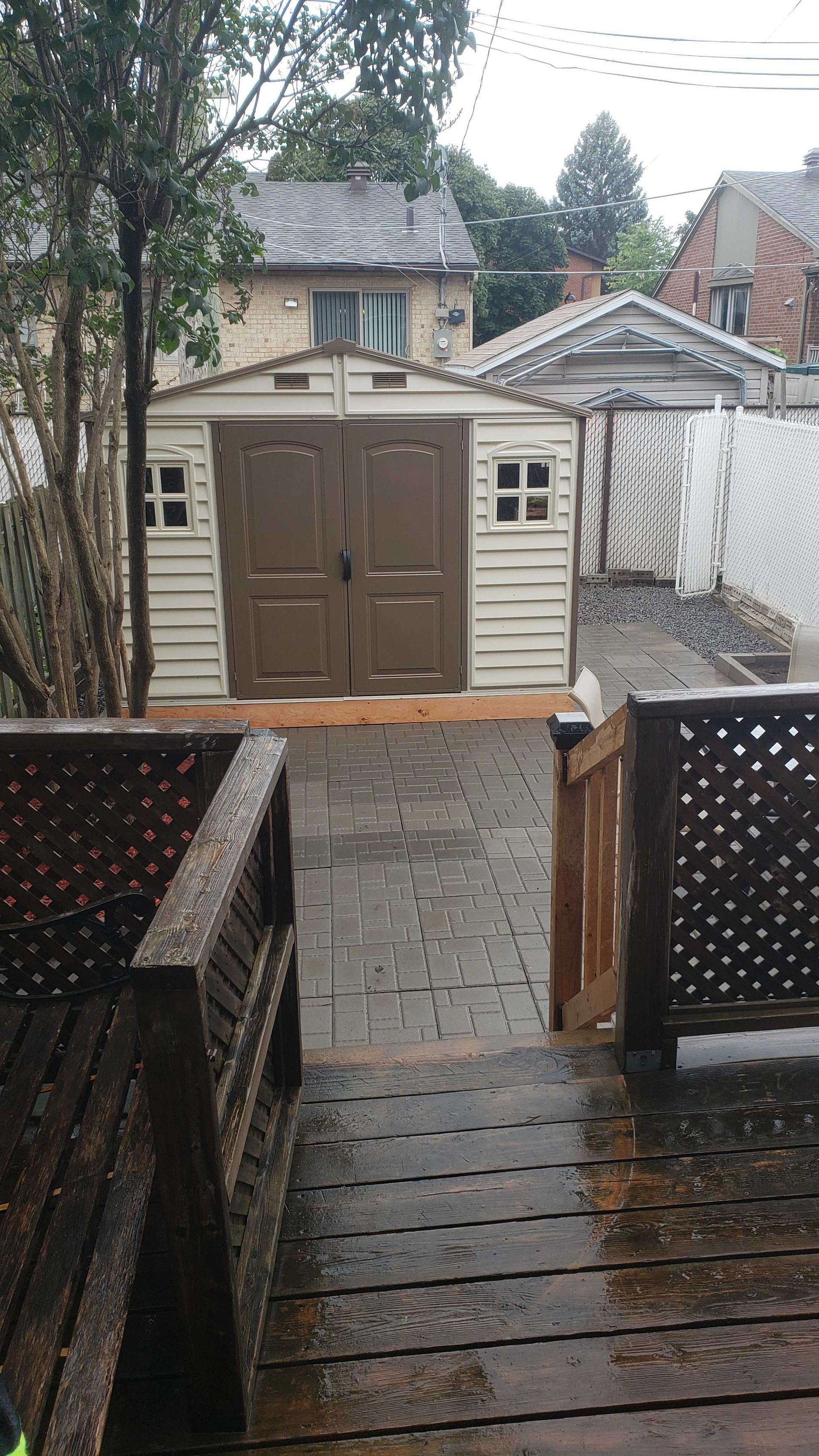 Terrasse arrière pluvieuse menant à un abri beige avec double porte et petites fenêtres