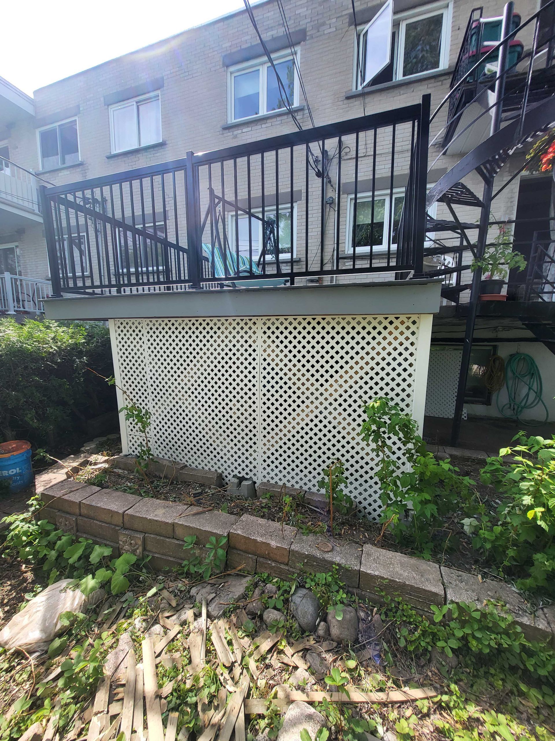 Balcon d'appartement avec rambarde noire surplombant un niveau inférieur recouvert d'un treillis blanc et une bordure de jardin en pierre