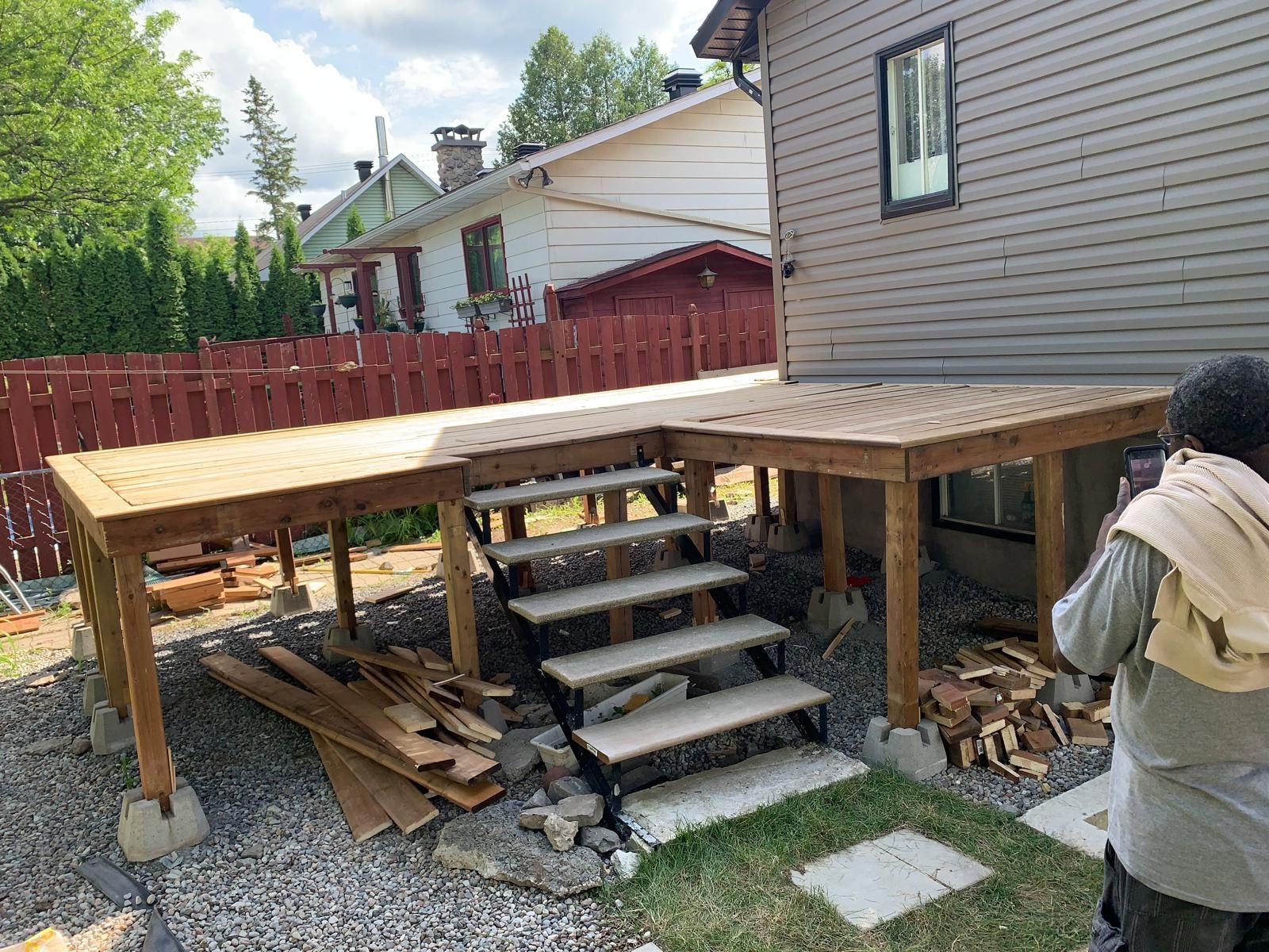 Une terrasse en construction se trouve à côté d'une maison, dans le jardin, avec des marches et du bois empilé en dessous.