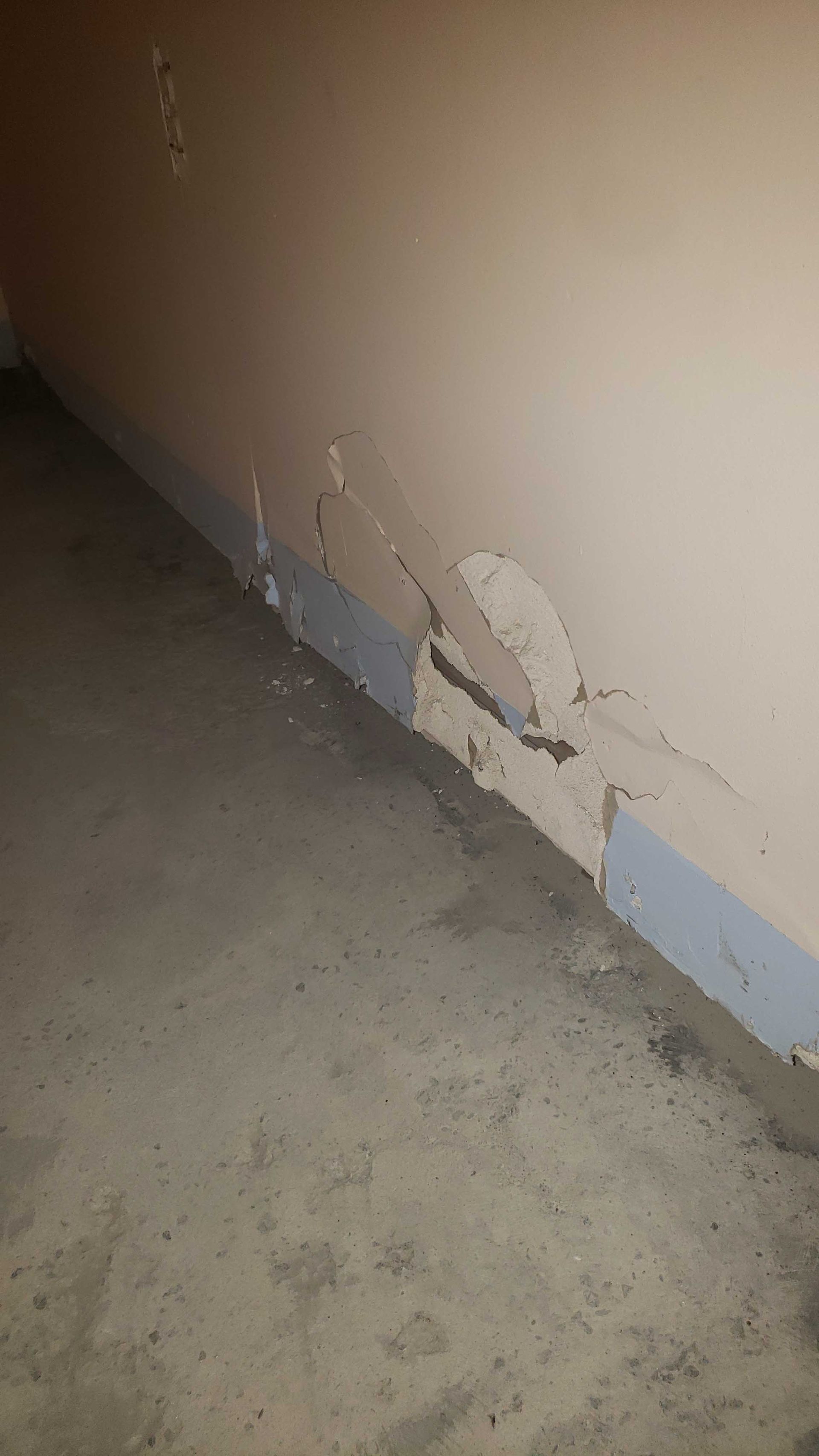 Coin de mur endommagé avec peinture écaillée et fissures au-dessus d'un sol en béton