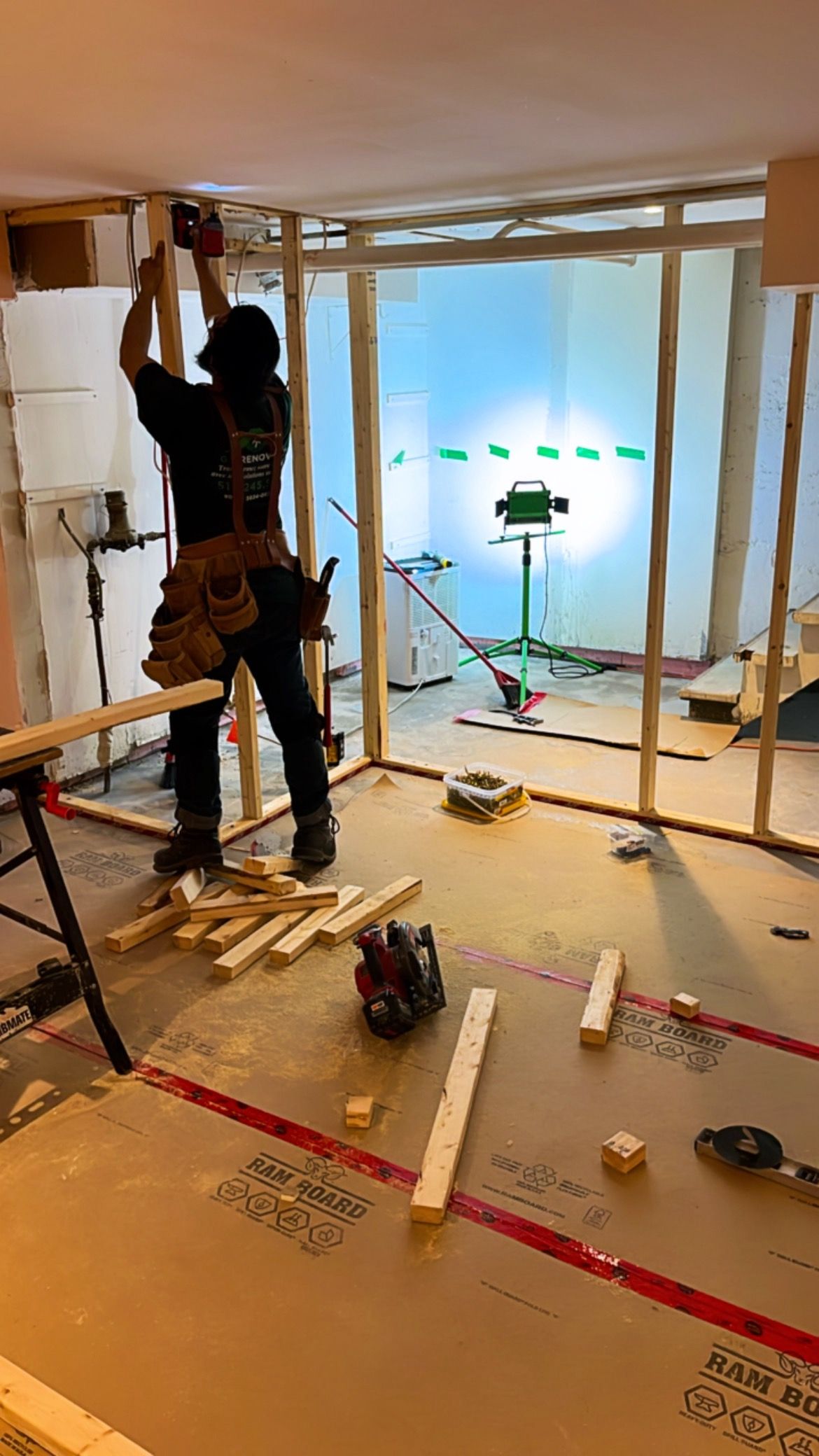 Rénovation intérieure en cours : un ouvrier installe un cadre en bois près d’une grande fenêtre lumineuse.