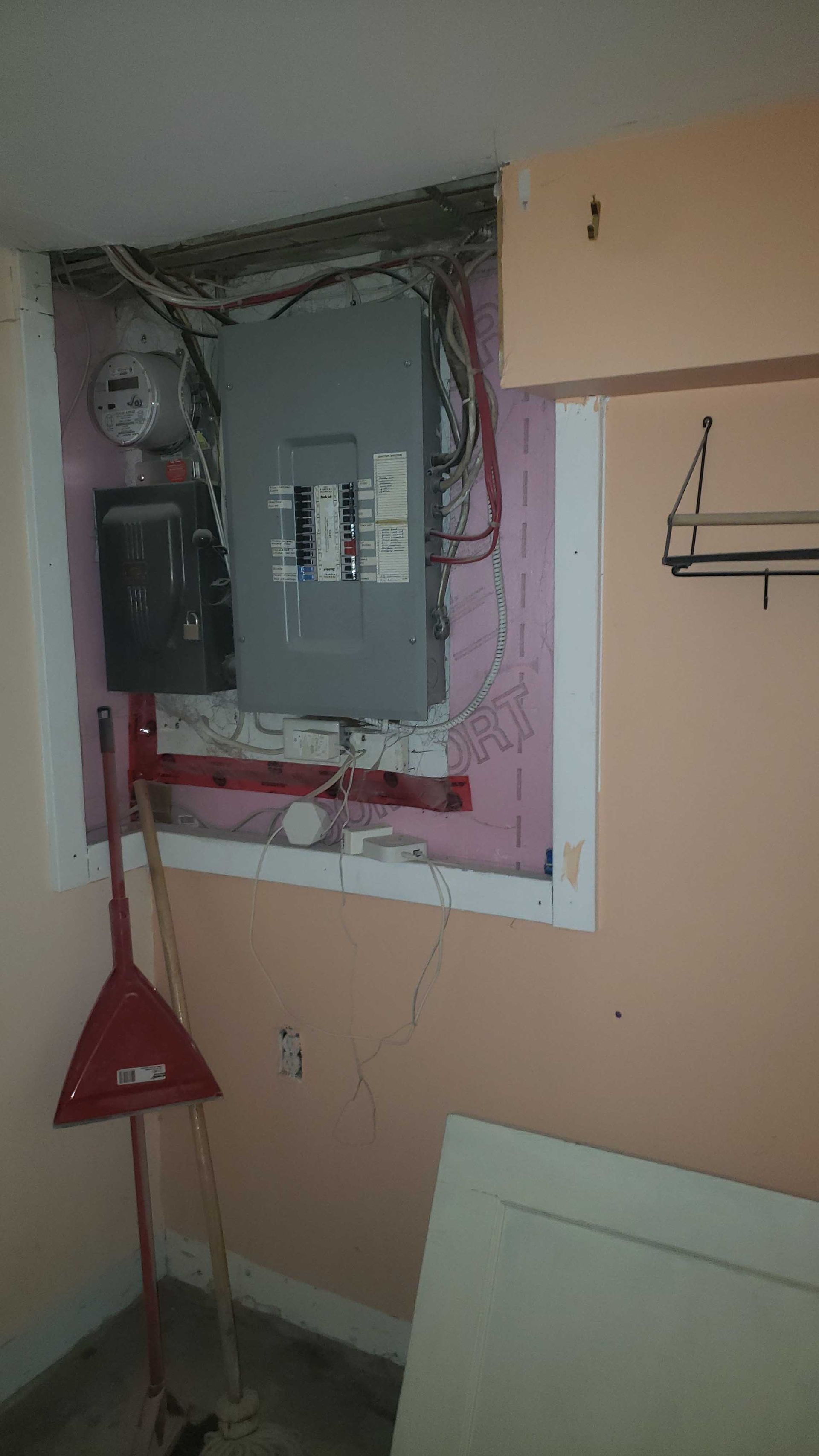 Panneau électrique ouvert sur le mur, avec fils apparents et panneau d'avertissement rouge à proximité.