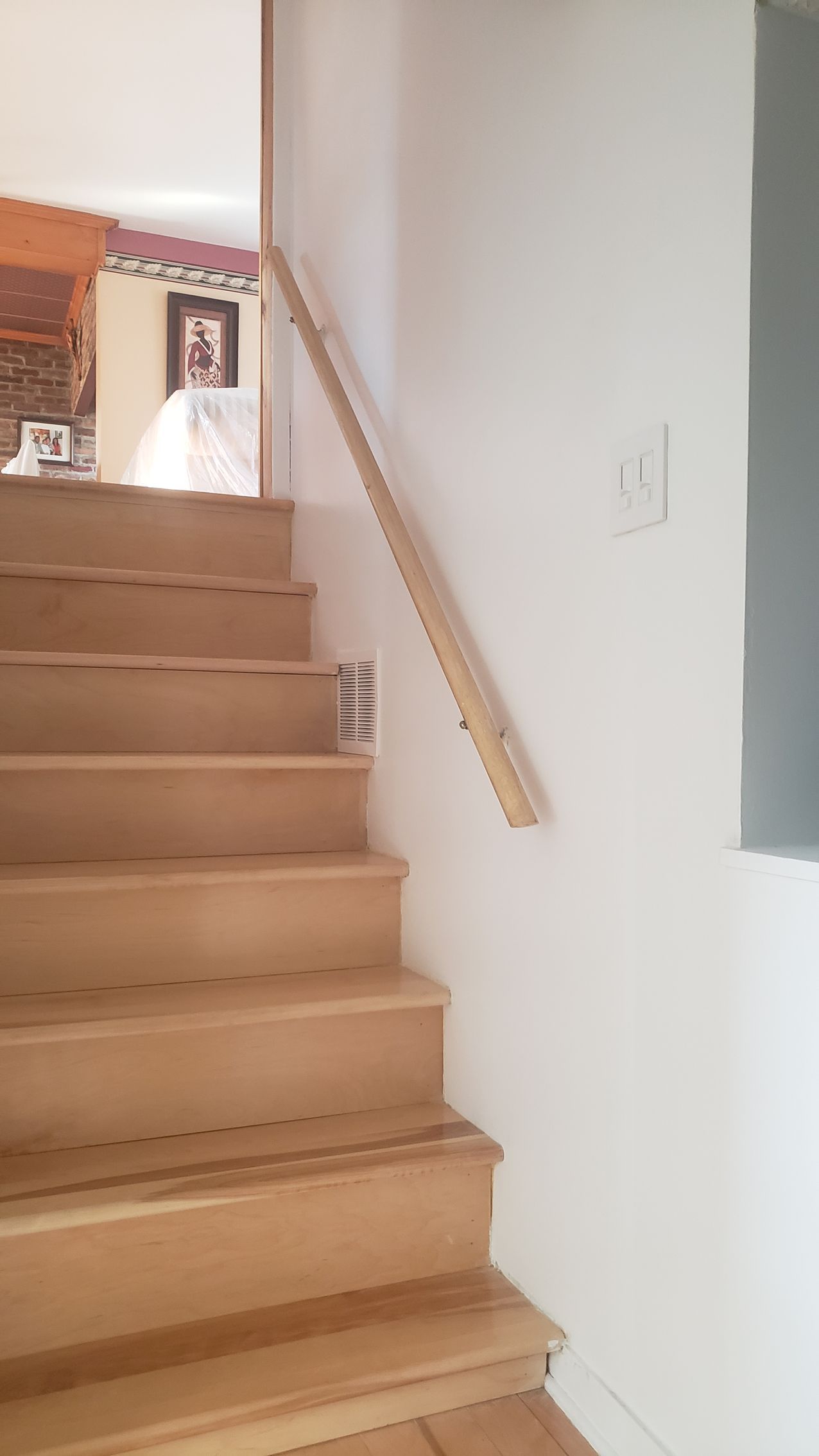 Escalier intérieur avec moquette beige, murs blancs et rampe en bois menant à un palier