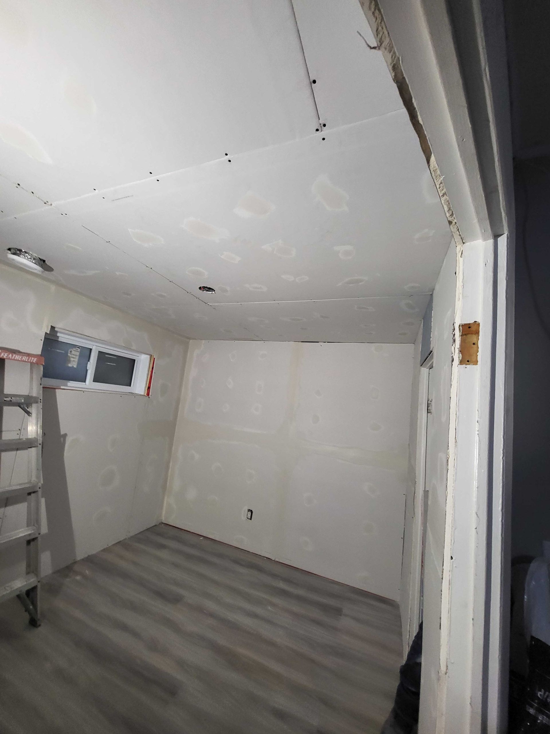 Pièce vide et inachevée avec des murs blancs, un sol gris et des zones de plafond apparentes.