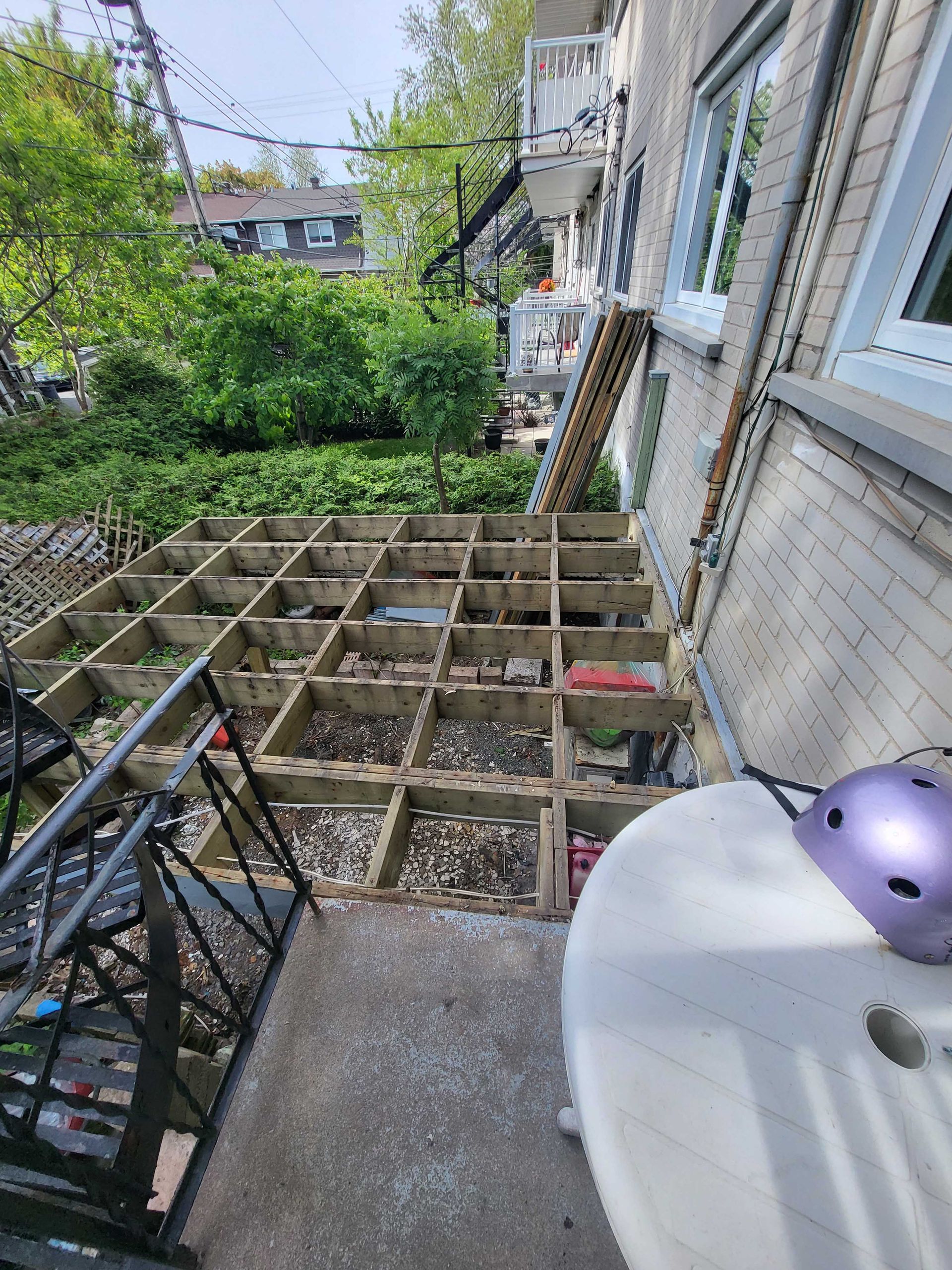 Terrasse arrière attenante à une maison, avec une structure de terrasse en bois en construction et une table blanche au premier plan.