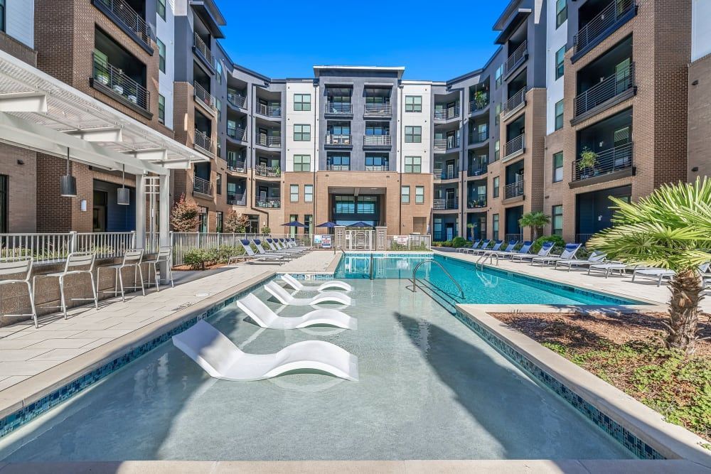 Outdoor swimming pool area in a modern apartment complex with loungers and surrounded by multi-story residential buildings under a clear blue sky at Marq at Crabtree in Raleigh, NC.