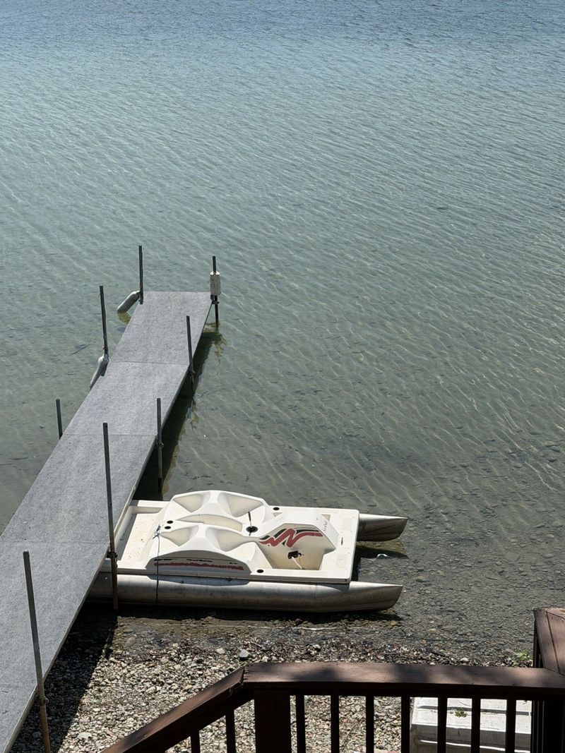 Dock extends into lake with kayaks, trees and cloudy sky.