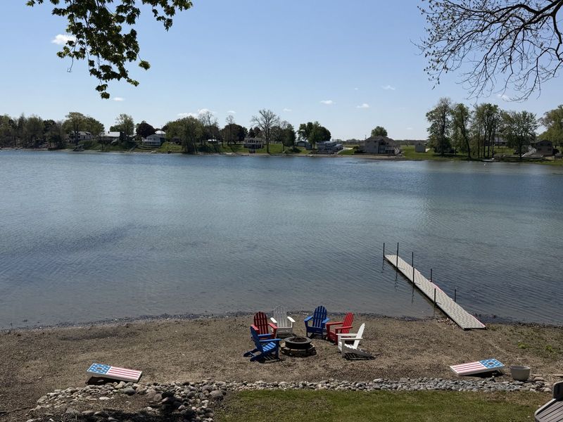 A light-colored house with a swing, path, and a lake view, on a grassy lot.