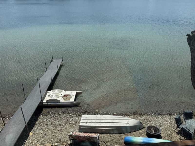 Dock extends into lake with kayaks, trees and cloudy sky.