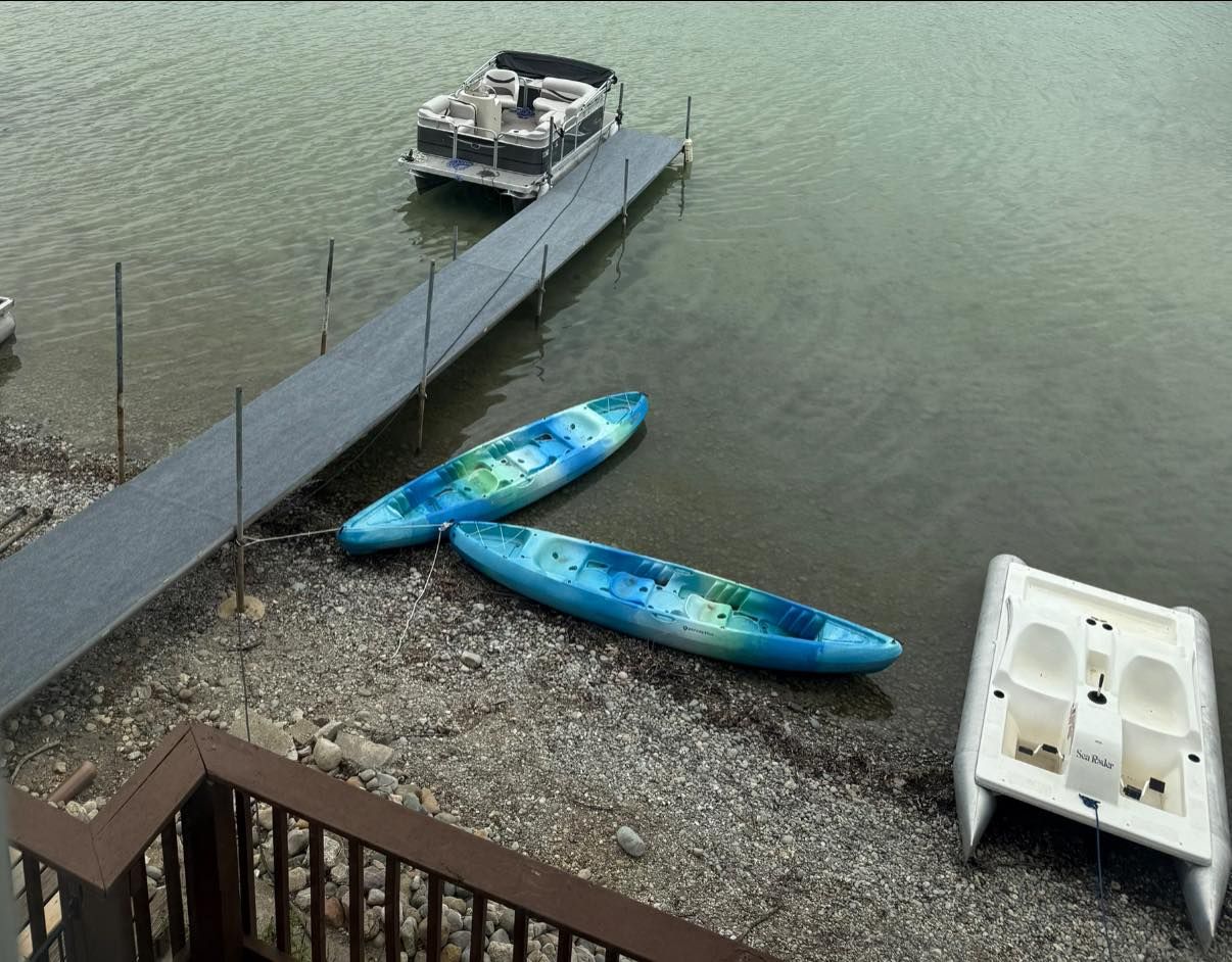 Two blue kayaks and a white paddle boat beside a dock on calm water