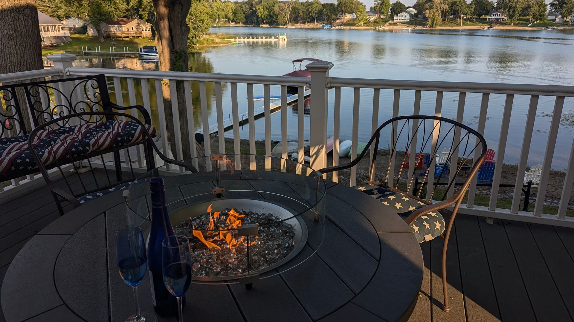 Deck with fire pit, chairs, and a lake view at sunset