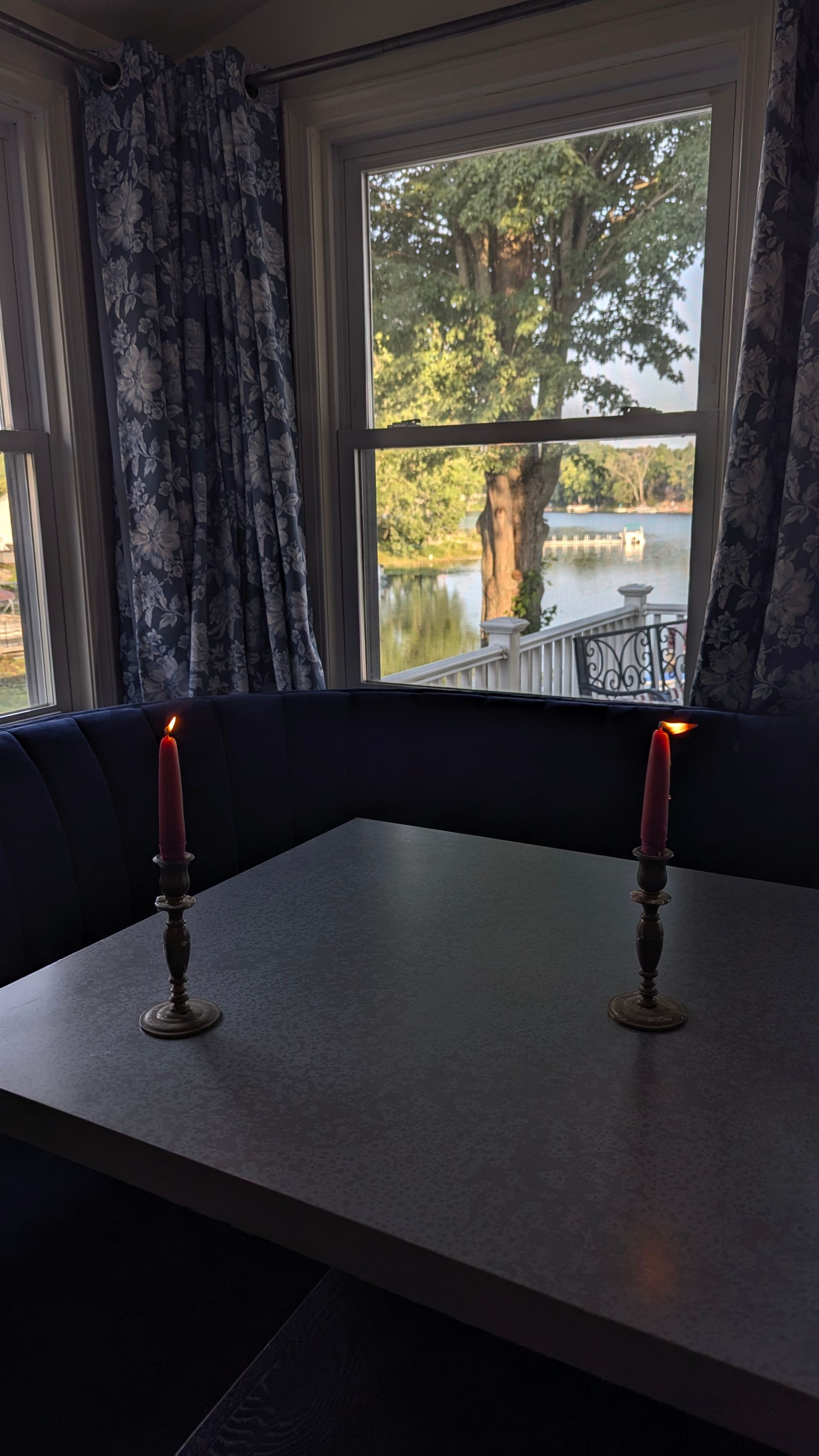 Dining table by a window with two lit red candles and a view of trees and rooftops outside