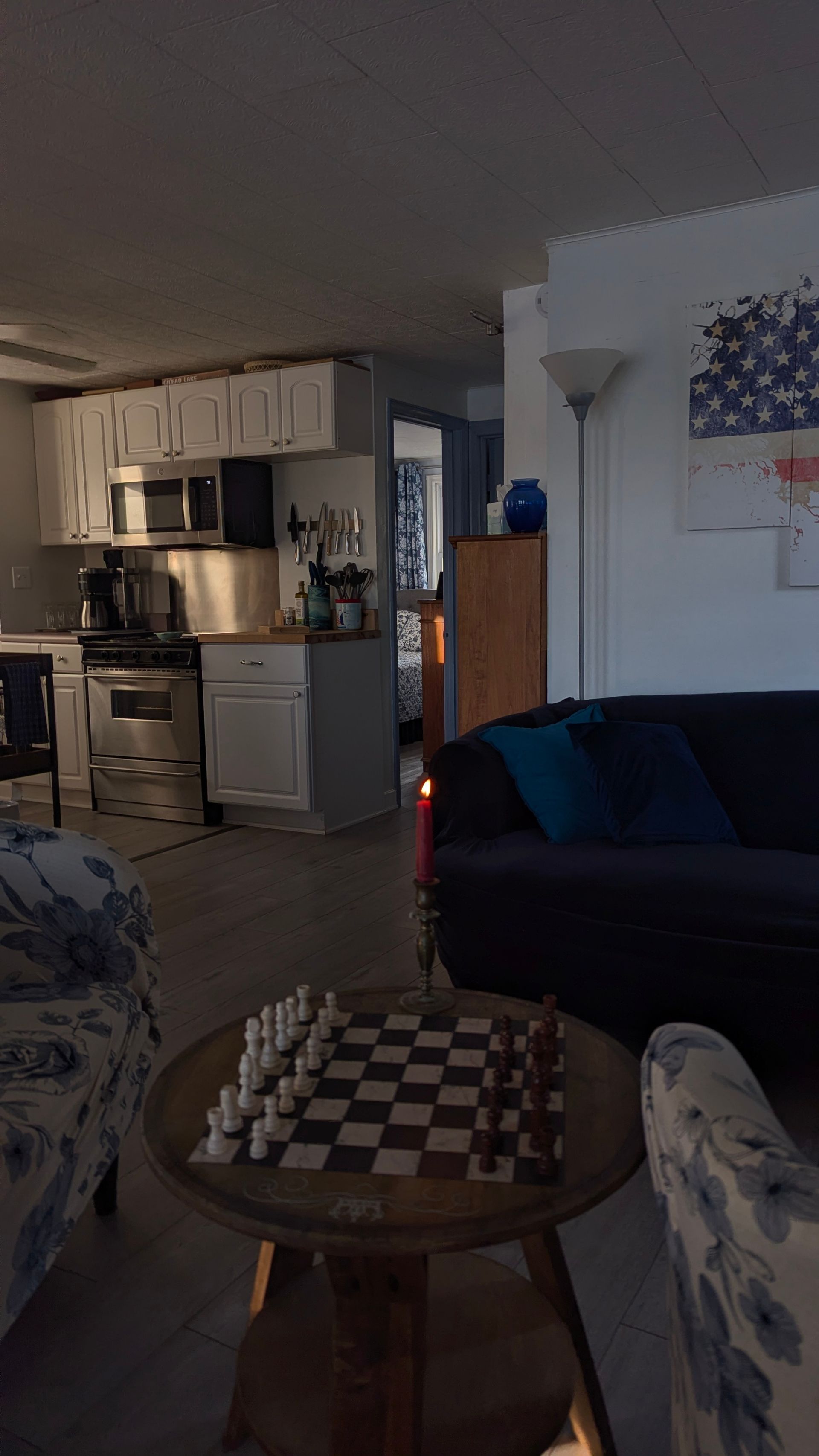 Cozy living room with a chessboard table, sofa, floor lamp, and open kitchen in the background