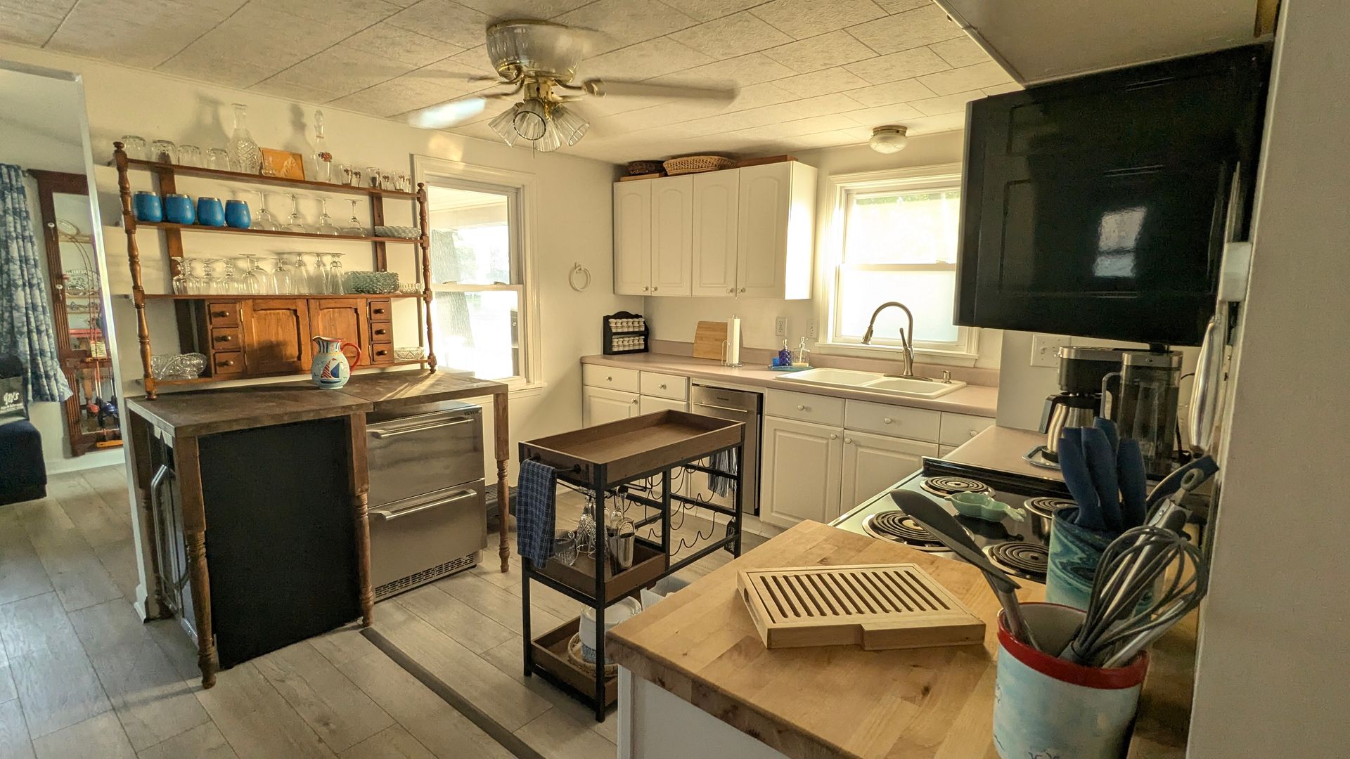 Cluttered kitchen with cabinets, island, sink, TV, and scattered tools and household items.