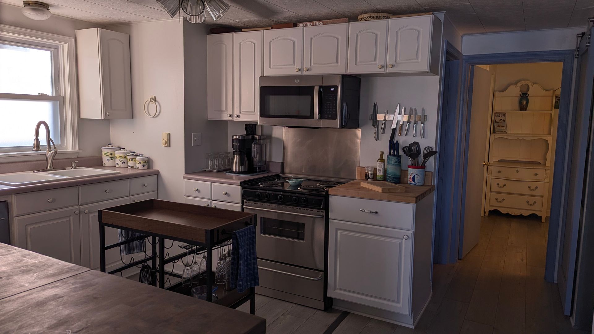 Modern kitchen with white cabinets, stainless steel appliances, and a central island by a window.