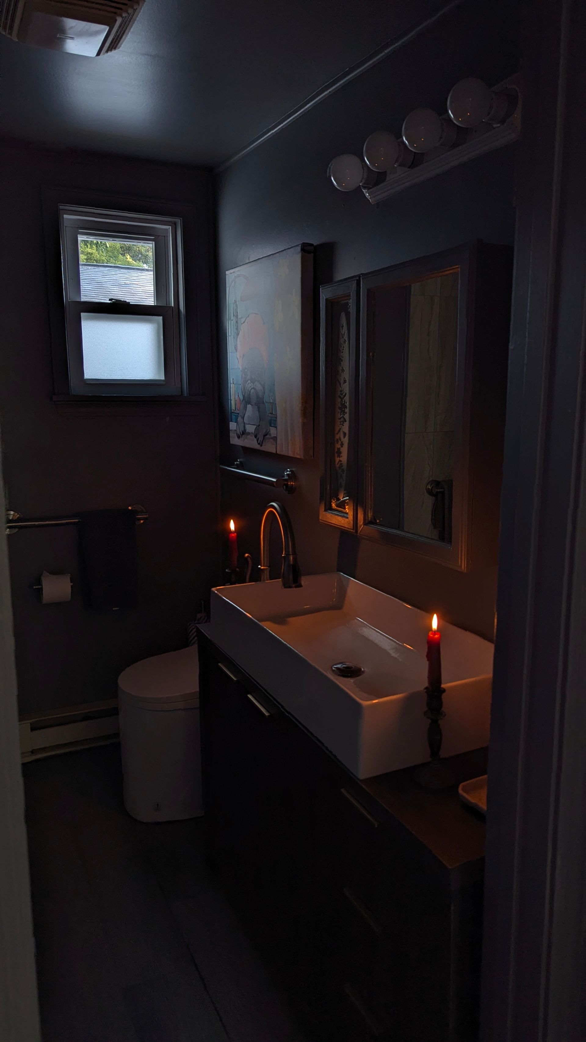 Dim bathroom with a sink, mirror, and lit candles creating a warm, spa-like atmosphere