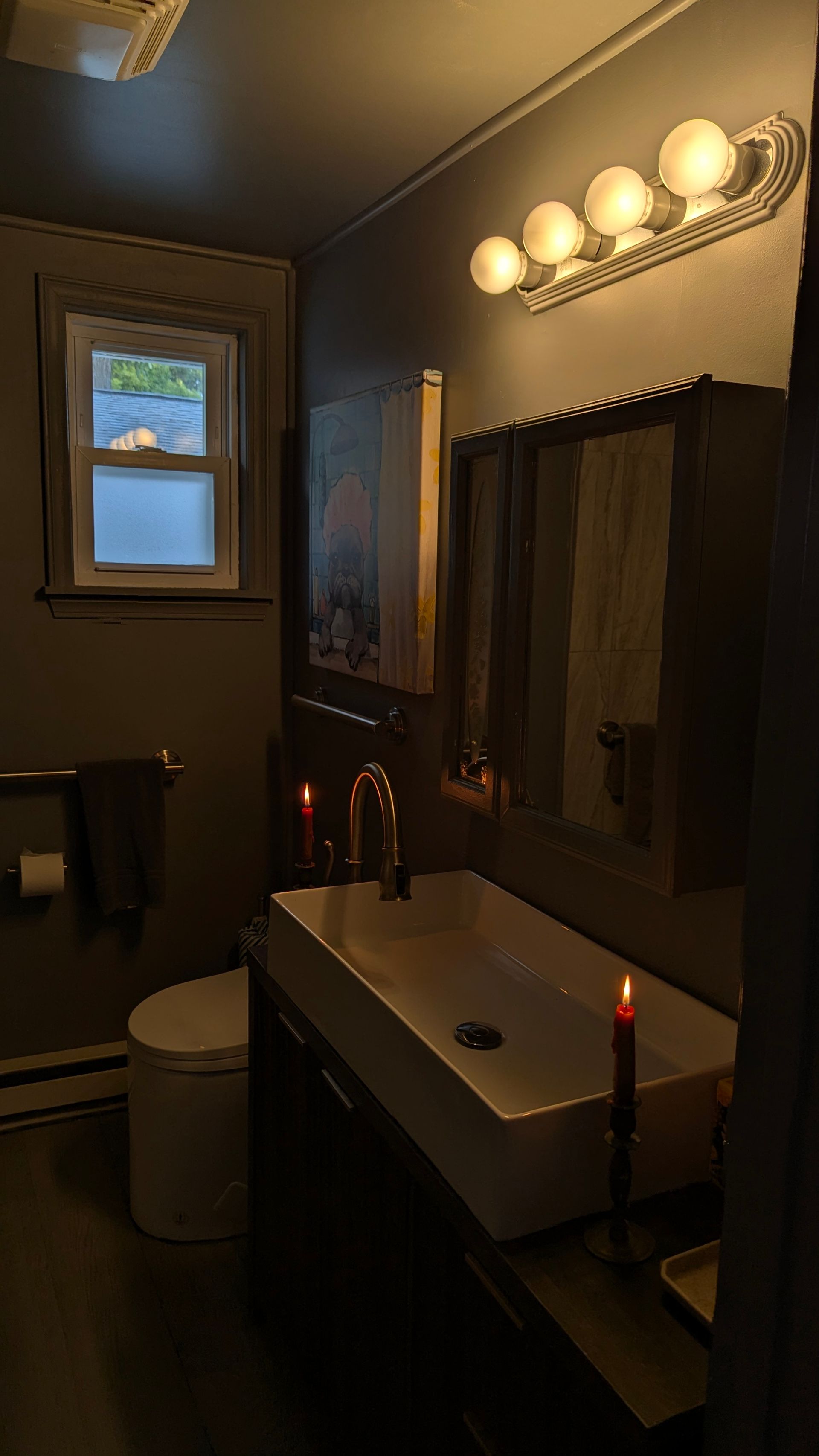 Dim bathroom with a sink, mirror lights, and candles on the counter.