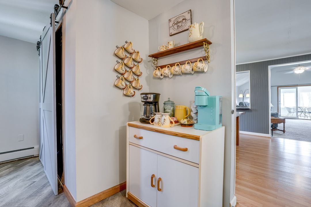 Coffee station with cabinet, coffee maker, mugs, and shelves on a wall, doorway on the left, open to another room.