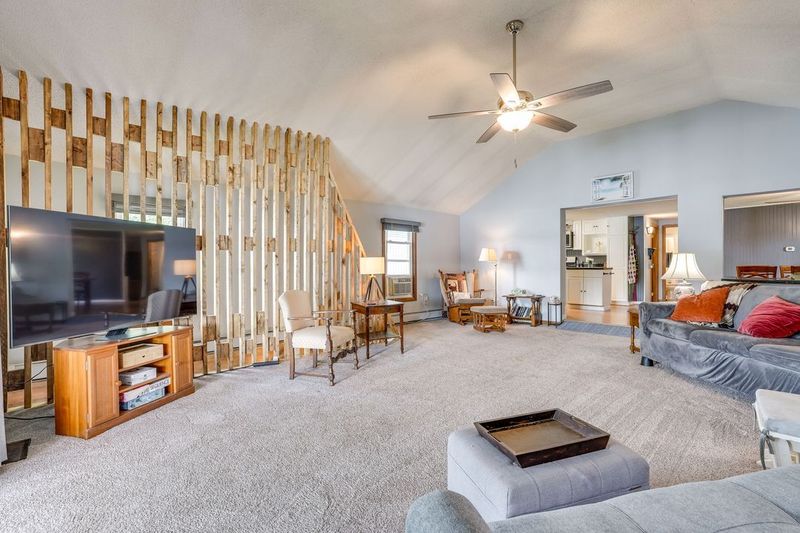 Living room with high ceiling, wood panel divider, large TV, sofa, chairs, and carpet.