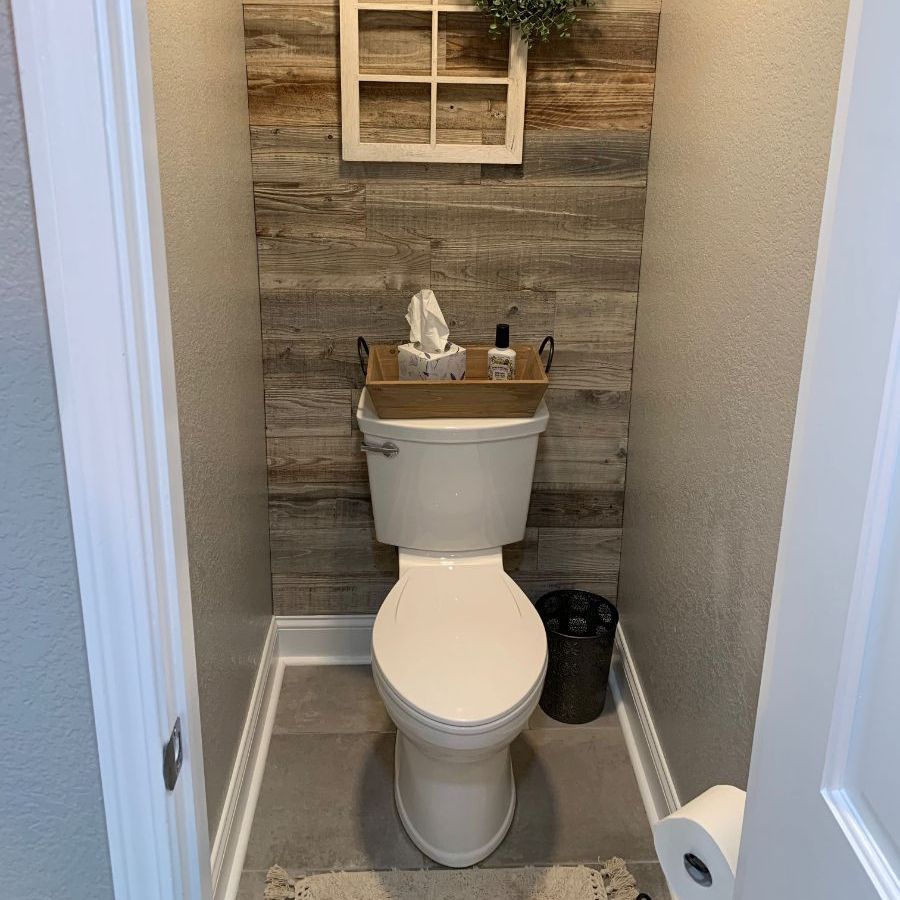 a toilet in a small bathroom with a wooden or tiled wall behind it .