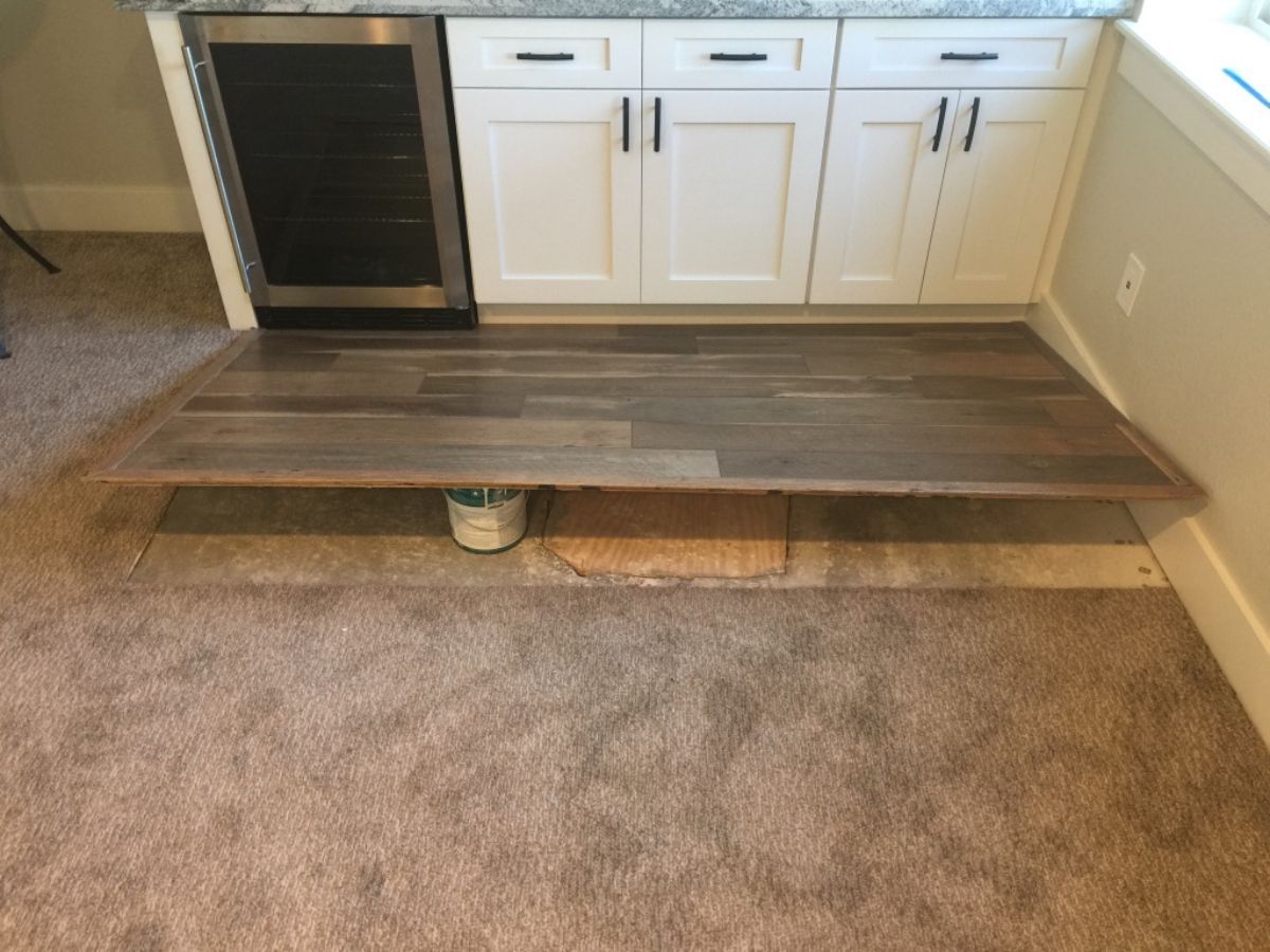 a kitchen with a wooden floor and white cabinets showing some custom drain work in the foundation