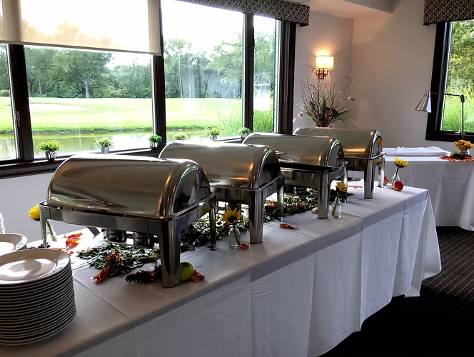 Buffet table with stainless steel food warmers, set up in a room with a window overlooking a pond.