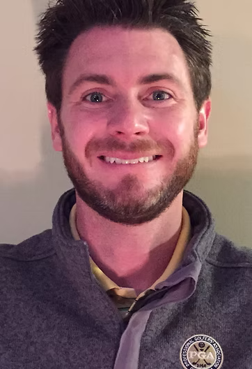 Smiling man in a gray pullover against a plain indoor background.