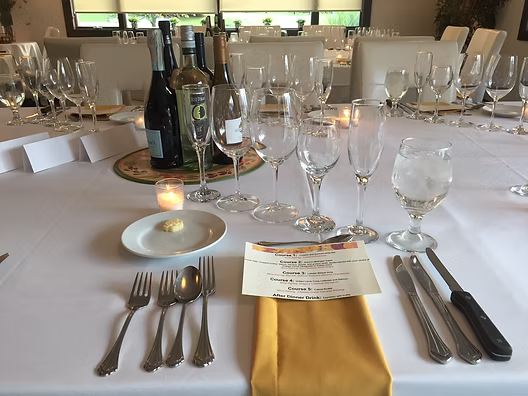 Formal table setting with wine bottles, glassware, silverware, and a menu.