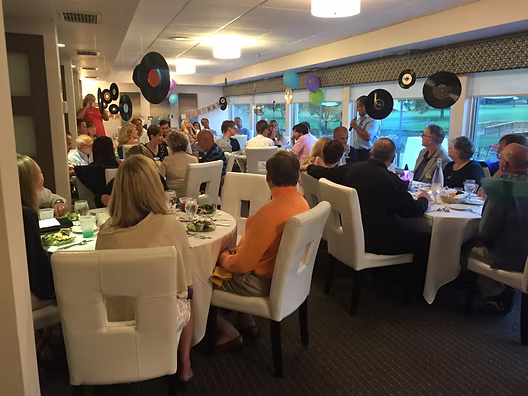 People at tables in a room, decorated with vinyl records and balloons, appear to be at a party or event.