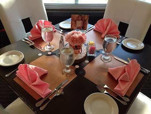 A dining table set for four with pink napkins, glassware, and a centerpiece.