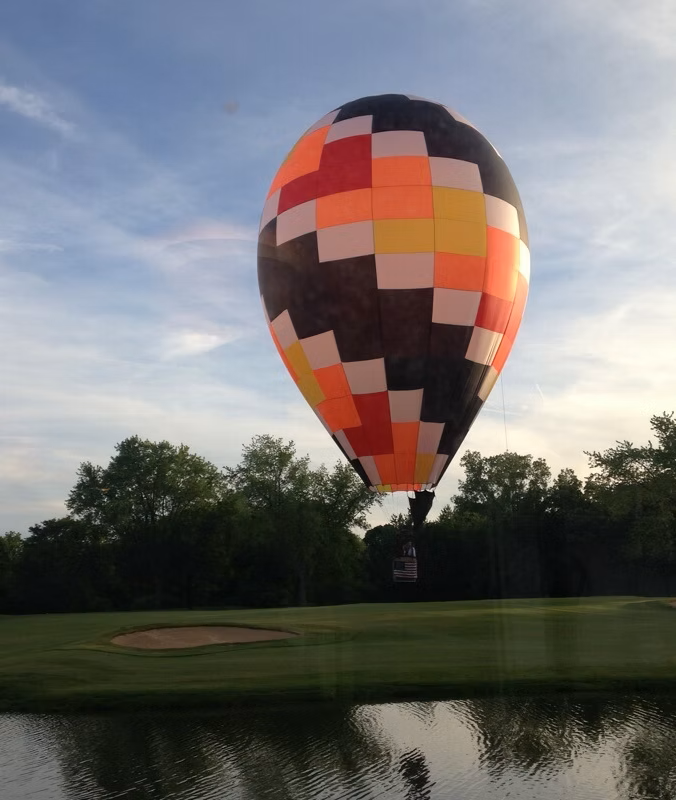 Hot air balloon with colorful patchwork design over a golf course and water.