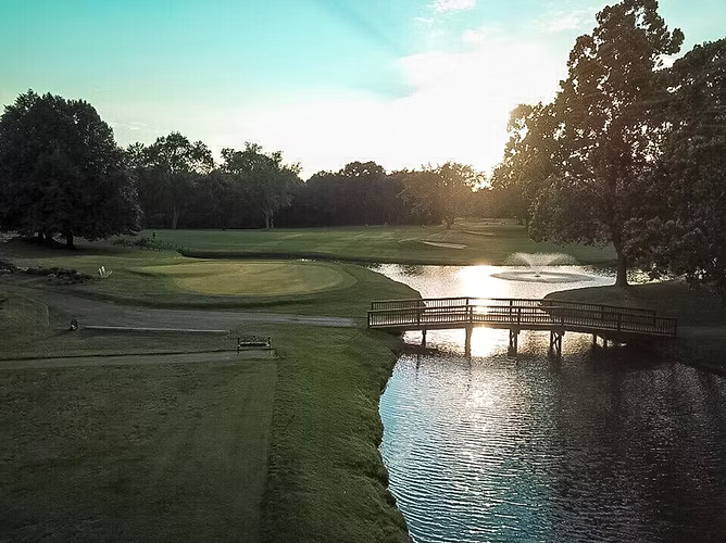 Golf course with water feature. A bridge crosses the water with the sun reflecting on the surface.