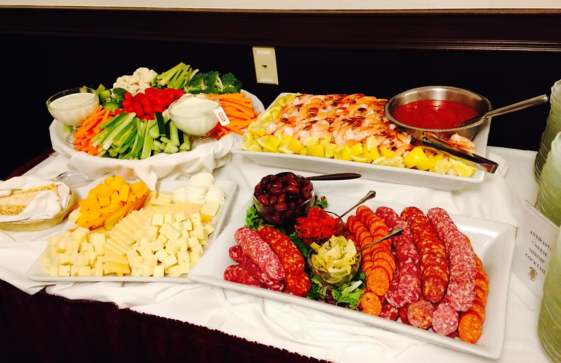 Buffet spread: vegetables, shrimp with cocktail sauce, cheeses, and cured meats.