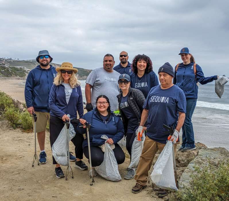 Group of people in blue shirts picking up trash on a coastal path.
