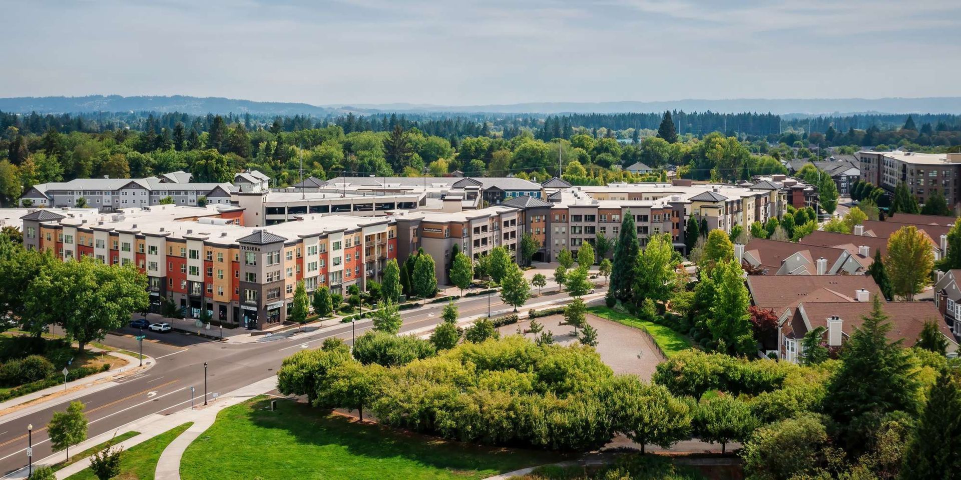 Aerial view of apartment buildings surrounded by trees and a road, with a distant mountain range.