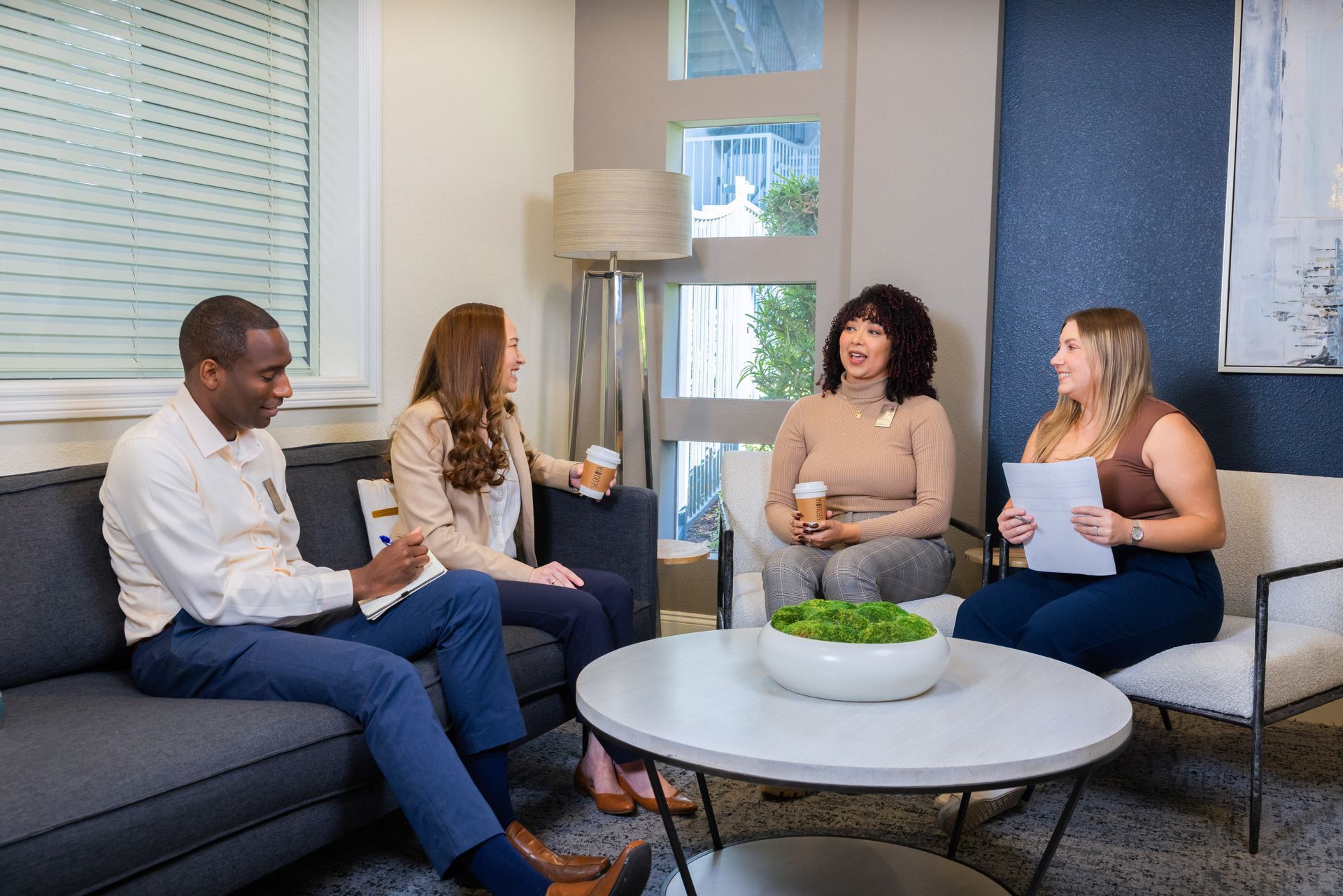 Four people in a modern living room setting. They are seated, smiling, and conversing around a coffee table.