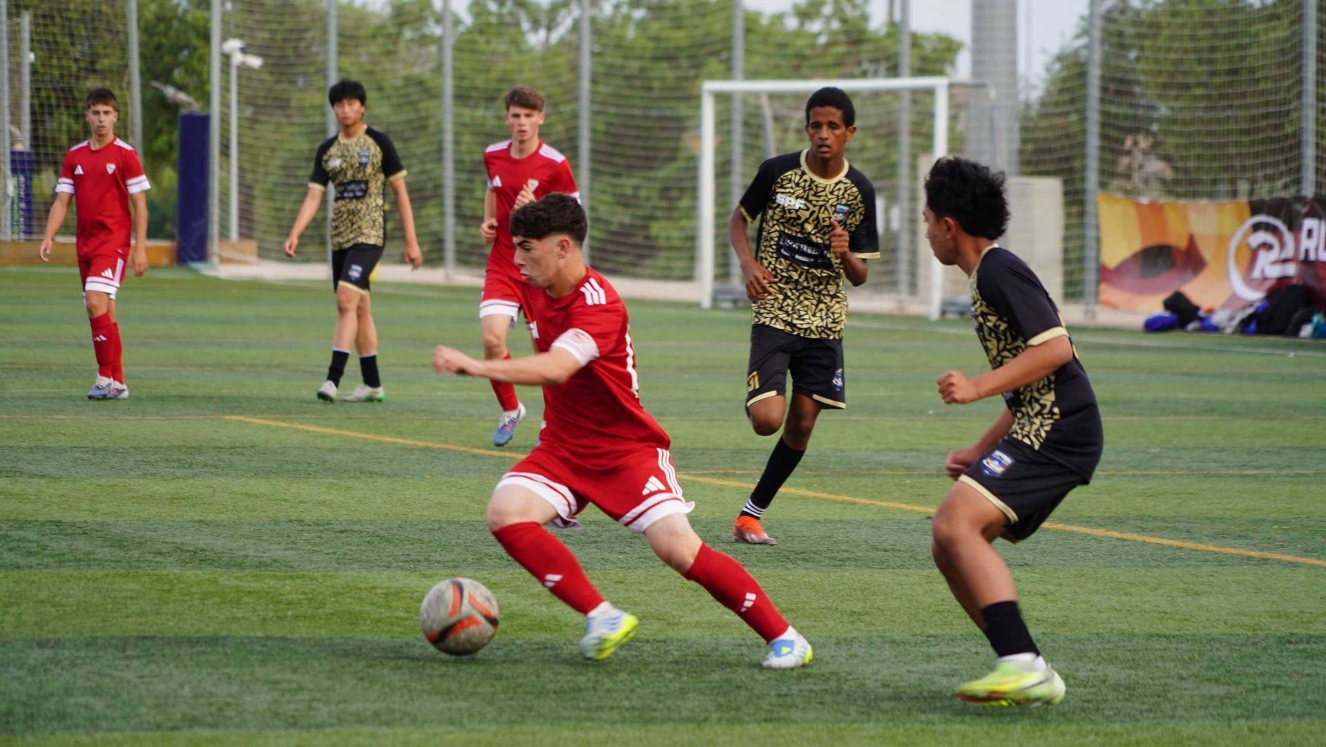 Soccer players in red and black uniforms contest the ball on an outdoor field