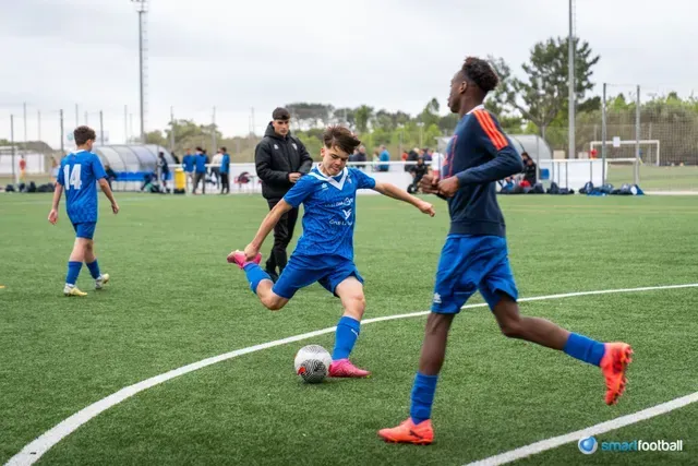 Soccer players in blue uniforms on a green field; one kicking a ball, others running.