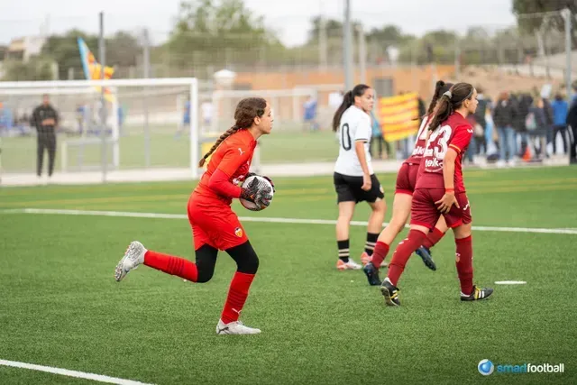 Female soccer player in red uniform runs with ball on green field.