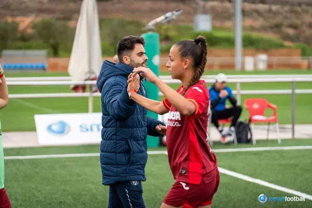Soccer player and coach on field, practicing. Player in red, coach in blue, green grass.