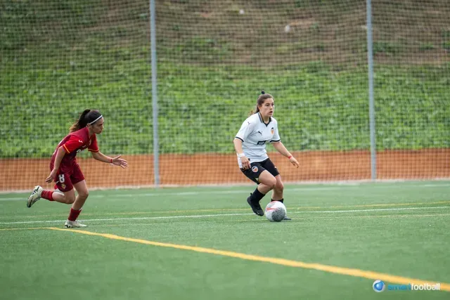 Soccer player in white jersey dribbles ball, chased by player in maroon jersey on green field.