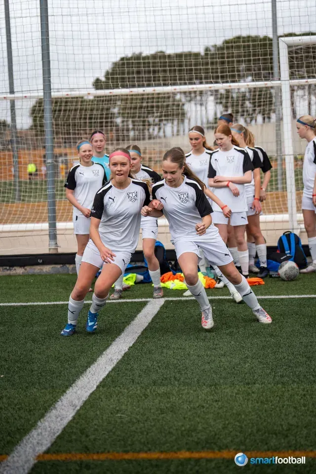 Soccer players in white and black uniforms, practicing footwork on a green field.