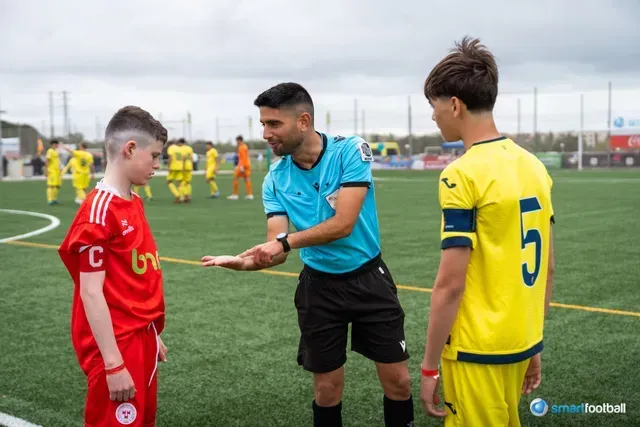 A soccer referee showing a card to players in red and yellow jerseys on the field.
